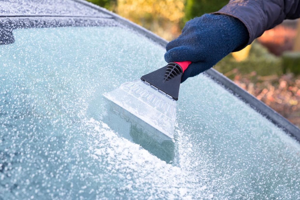Person using an ice scraper to scrape ice off of their car windshield