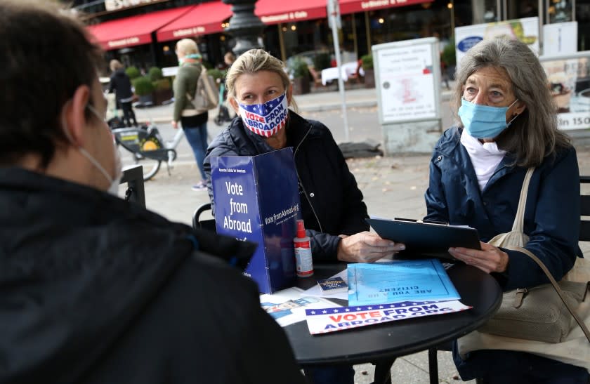 BERLIN, GERMANY - OCTOBER 10: Renee Johnsson of Democrats Abroad (C) and Florian Schiedhelm of Vote from Abroad (L) assist U.S. citizen Emily Schalk to register to vote absentee in the U.S. presidential elections to be held on November 3, at a Starbucks coffeeshop on October 10, 2020 in Berlin, Germany. Approximately 2.9 million Americans are eligible to vote from abroad, according to estimates from the Federal Voting Assistance Program. (Photo by Adam Berry/Getty Images)