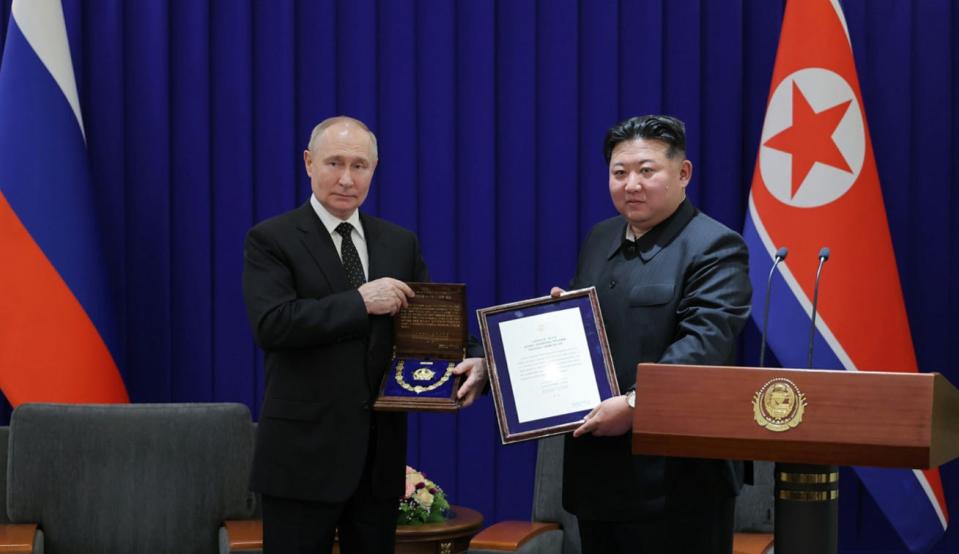 Vladimir Putin and Kim Jong Un hold an award bestowed to Putin.