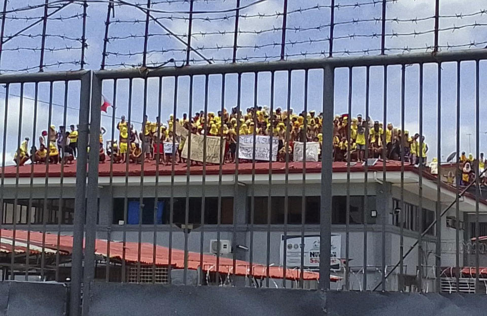 Filipino inmates stand on top of the roof of a prison building as they protest in Pototan town, Iloilo province, central Philippines on Wednesday Aug. 24, 2022. About 100 inmates in an overcrowded jail climbed atop the roof of a prison building in the central Philippines and noisily protested with raised fists and placards, saying they were not being fed well and demanding the removal of the jail warden, who was immediately suspended, jail officials said Thursday. (AP Photo/Fred Pasgala)