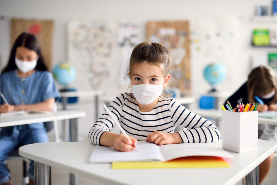 Front view portrait of child with face mask back at school after covid-19 quarantine and lockdown, writing.