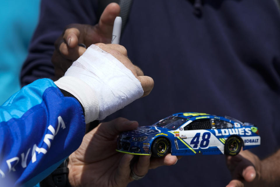 Chip Ganassi Racing driver Jimmie Johnson, left, of United States signs a model of his car for a fan before an IndyCar auto race at the Grand Prix of Long Beach on Sunday, April 10, 2022, in Long Beach, Calif. Johnson's right hand was injured in a crash on Friday. (AP Photo/Ashley Landis)