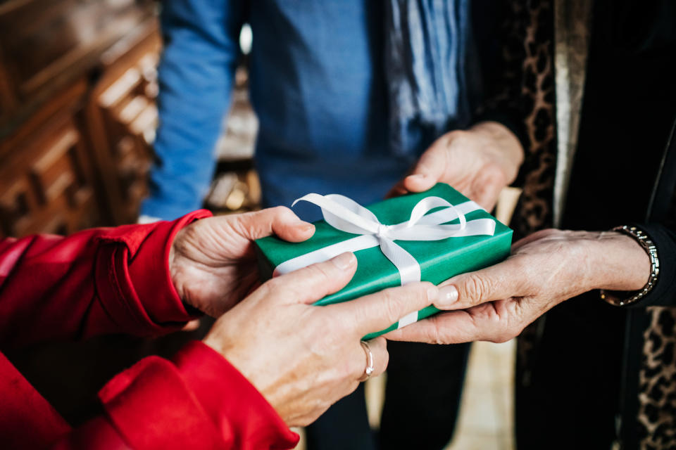 a mature woman presenting her friend with a birthday gift before sitting down for lunch in a restaurant together.