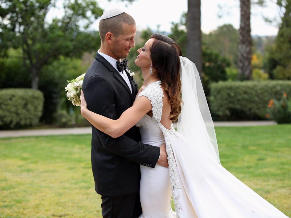 JP Rosenbaum, in a tuxedo and white yarmulke, embraces Ashley Hebert, in a white backless wedding dress and veil, on their wedding day in 2012.