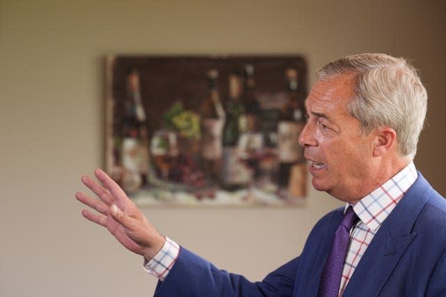 Nigel Farage, wearing a blue suit and purple tie, points with his right hand