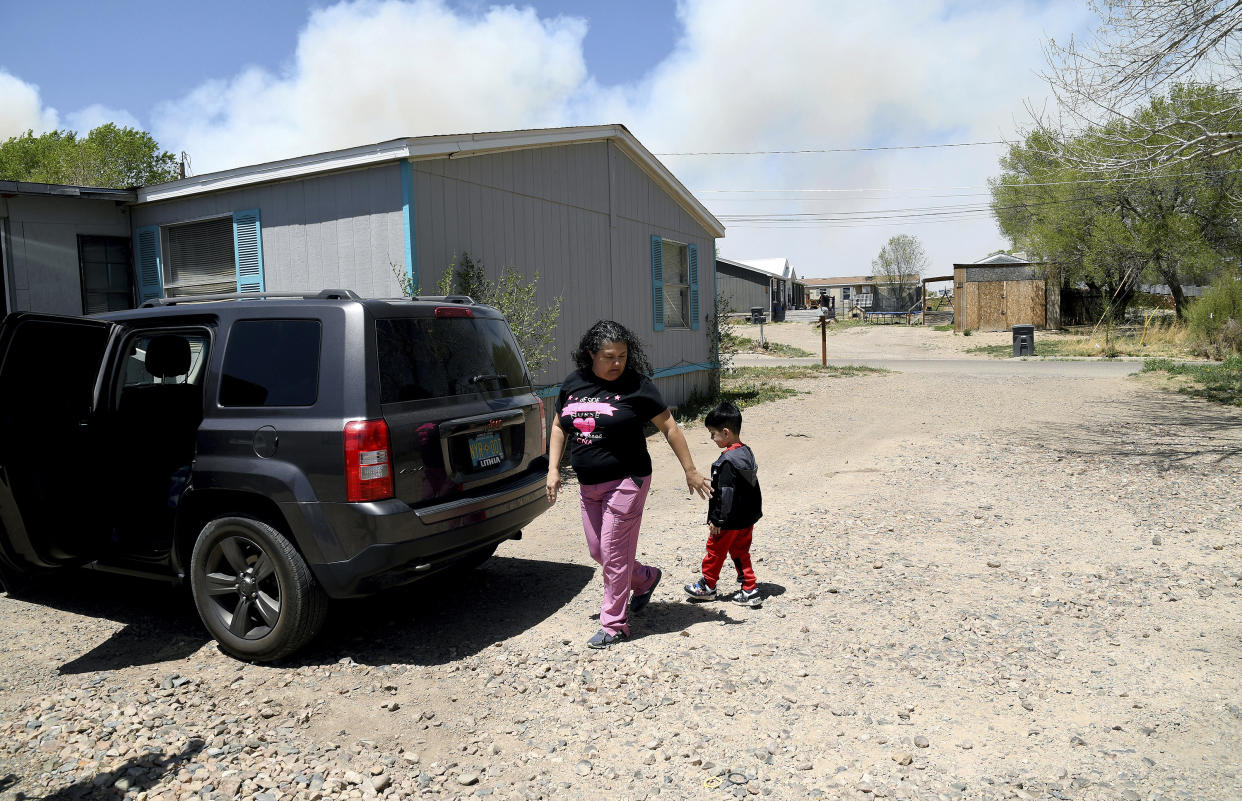 Martina Gonzales and her grandson, Lukas Lee Mora, 4, walk outside of their home in Las Vegas, N.M., as a plume of smoke rises in the distance Tuesday, May, 3, 2022. Flames raced across more of New Mexico's pine-covered mountainsides Tuesday, charring more than 217 square miles (562 square kilometers) over the last several weeks. Gonzales and her husband have packed up their valuables and are ready to leave the area if the fire tops the ridge behind their house. (AP Photo/Thomas Peipert)