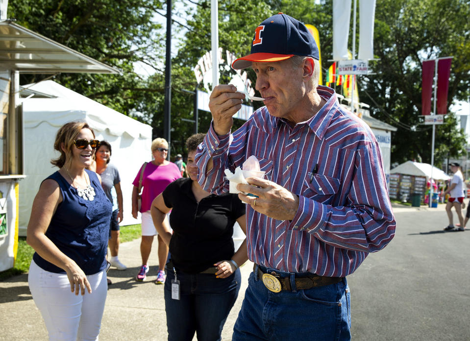 FILE--In this Aug. 9, 2018, file photo, Illinois Gov. Bruce Rauner eats strawberry ice cream while walking on the Illinois State Fairgrounds after officially opening the 2018 Illinois State Fair in Springfield, Ill. Gubernatorial fashion in Illinois gets a lot of attention. Rauner eschewed neckties with suits, wore big belt buckles, plaid shirts with rhinestone snaps, and a leather vest while astride his motorcycle. (Rich Saal /The State Journal-Register via AP, File)