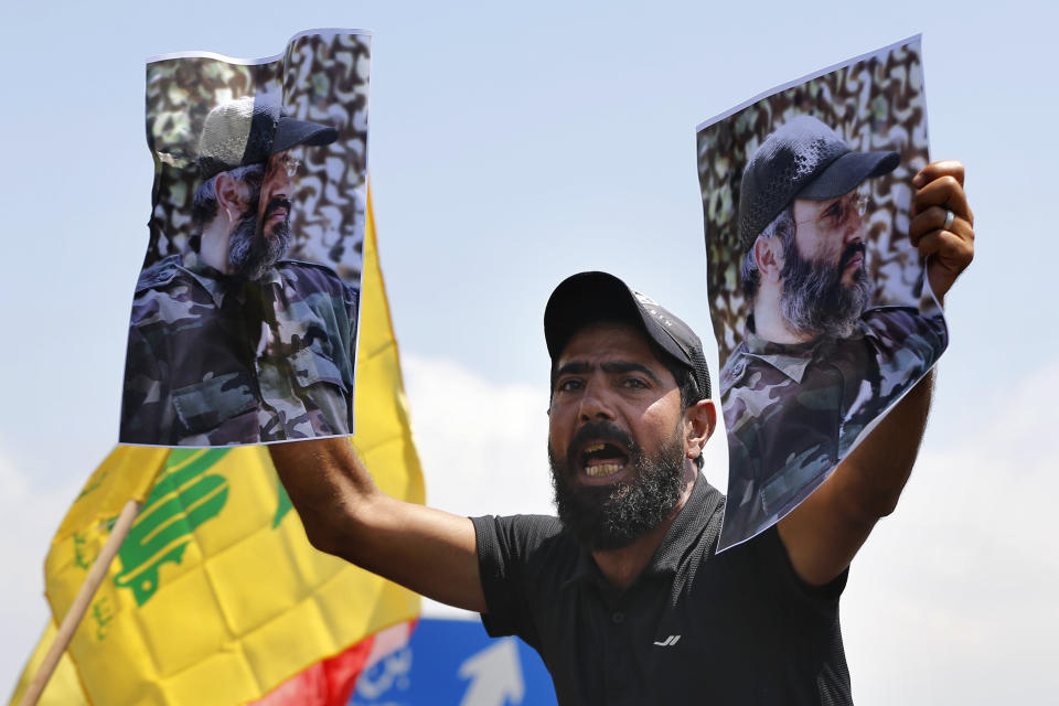 FILE - In this July 8, 2020 file photo, a Hezbollah supporter chant slogans and hold posters of the late Hezbollah military commander Imad Mughniyeh, while protesting the visit to Lebanon by Gen. Frank McKenzie, the head of U.S. Central Command, outside ​​the Rafik Hariri International Airport in Beirut, Lebanon. For many, the Iran-backed Hezbollah now stands at the top of Lebanon’s sectarian-based system of power — and so is complicit in the corruption many blame for the port disaster and for driving the country into near bankruptcy. (AP Photo/Bilal Hussein, File)