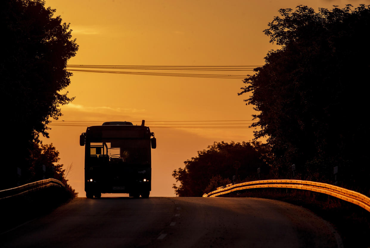 An empty bus comes along a land road in Frankfurt, Germany, as the sun rises Wednesday, May 13, 2020. (AP Photo/Michael Probst)