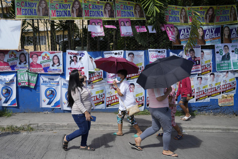 Voters pass by campaign posters outside a polling center Monday, May 9, 2022 in Quezon City, Philippines. Filipinos were voting for a new president Monday, with the son of an ousted dictator and a champion of reforms and human rights as top contenders in a tenuous moment in a deeply divided Asian democracy. (AP Photo/Aaron Favila)