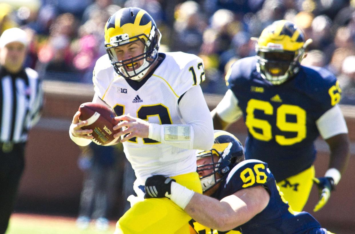 Michigan quarterback Alex Malzone (12) is tackled by defensive lineman Ryan Glasgow (96) during a spring NCAA college football game in Ann Arbor, Mich., Saturday, April 4, 2015. (AP Photo/Tony Ding)