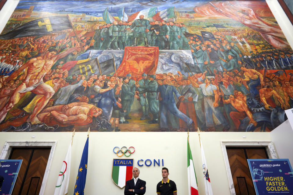 FILE - Italian Olympic Committee (CONI) President Giovanni Malago', bottom left, and Italian athlete Filippo Tortu attend a press conference to present the Golden Gala athletic meeting, as they stand beneath a mural titled "Apotheosis of Fascism", in the Salone d'Onore of the CONI headquarters, in Rome, Tuesday, May 14, 2019. Italy's failure to come to terms with its fascist past is more evident as it marks the 100th anniversary, Friday, Oct. 28, 2022, of the March on Rome that brought totalitarian dictator Benito Mussolini to power as the first postwar government led by a neo-fascist party takes office. (AP Photo/Andrew Medichini, File)