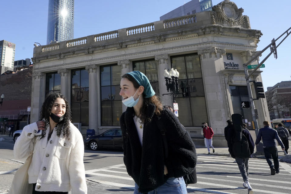 Passers-by wear masks under their chins as they chat with one another while crossing a street, in Boston, Wednesday, Feb. 9, 2022. Students and staff at public schools in Massachusetts will no longer be required to wear face coverings while indoors starting Feb. 28. Americans who have been clamoring for an end to mask-wearing have welcomed new guidance from the Centers for Disease Control and Prevention. It says healthy people in most areas of the country can safely stop wearing masks. (AP Photo/Steven Senne)