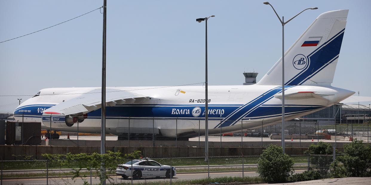 massive cargo jet behind fence, small looking police car on street in front of it