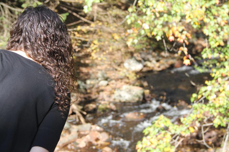 A woman leaning over to look into a gushing brook.