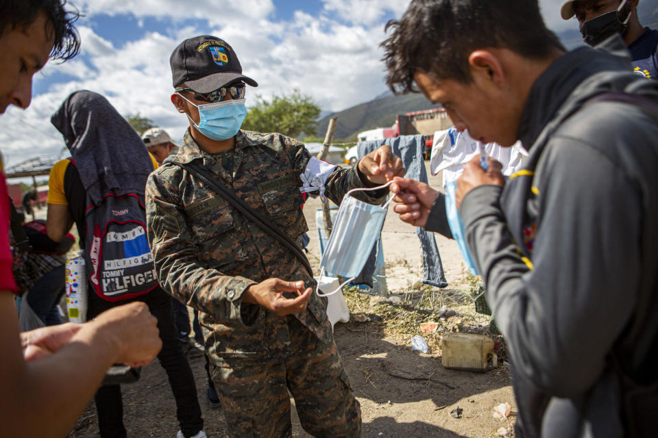 A member of the Guatemalan army hands a protective face mask to an Honduran migrant who has been detained at a police checkpoint on the border near Zacapa, Guatemala, Wednesday, Jan. 20, 2021. After a year of pandemic-induced paralysis, those in daily contact with migrants believe the flow north could return to the high levels seen in late 2018 and early 2019. The difference is that it would happen during a pandemic. (AP Photo/Oliver de Ros)