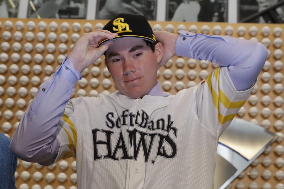 SoftBank Hawks pitcher Carter Stewart Jr. puts on the team's hat during a baseball news conference in Newport Beach, Calif., Thursday, May 30, 2019. After failing to sign with Atlanta and losing a grievance against the Braves, 19-year-old right-hander Carter Stewart has agreed to a six-year contract with the Fukuoka SoftBank Hawks of Japan's Pacific League. (AP Photo/Chris Carlson)