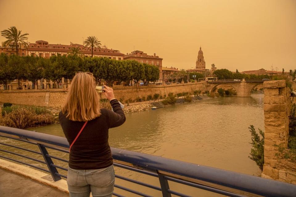 A woman takes a photo of the downtown of Murcia, Spain orange-blanketed with heavy dust this week (EPA)