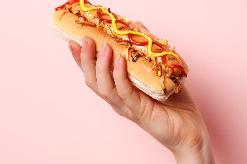 Young female hand holding American style hotdog on a pastel pink background