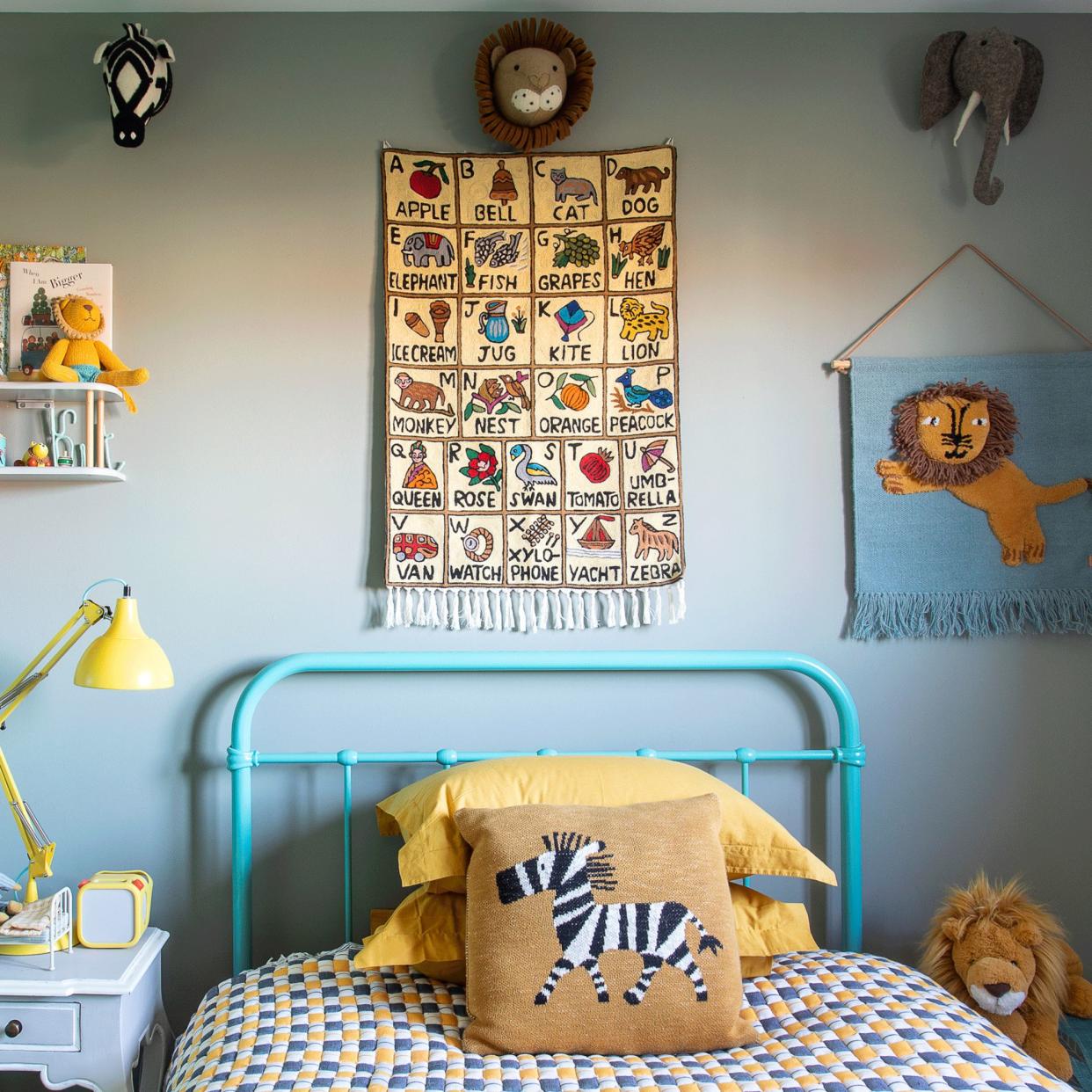  A kid's bedroom painted pale blue with yellow accents, including a bedside lamp, zebra cushion, lion tapestry and alphabet poster. 
