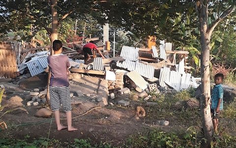 An Indonesian person scrambles over the collapsed ruins of a house as others look on following an earthquake in Lombok - Credit: AFP