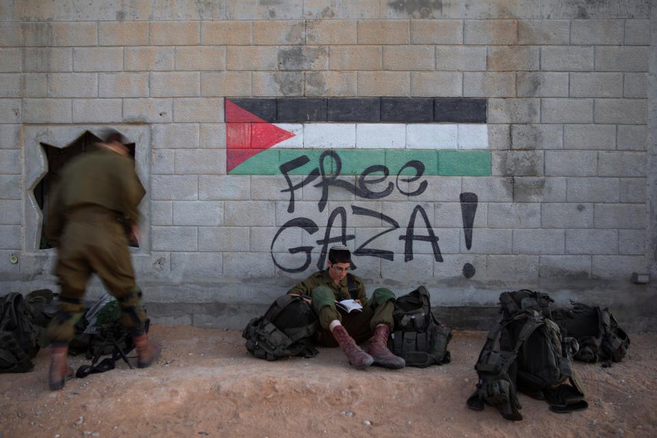 An Israeli soldier reads from a book next to graffiti featuring the Palestinian flag, during an urban warfare exercise in an army training facility at the Zeelim army base, southern Israel, Nov. 9, 2021.