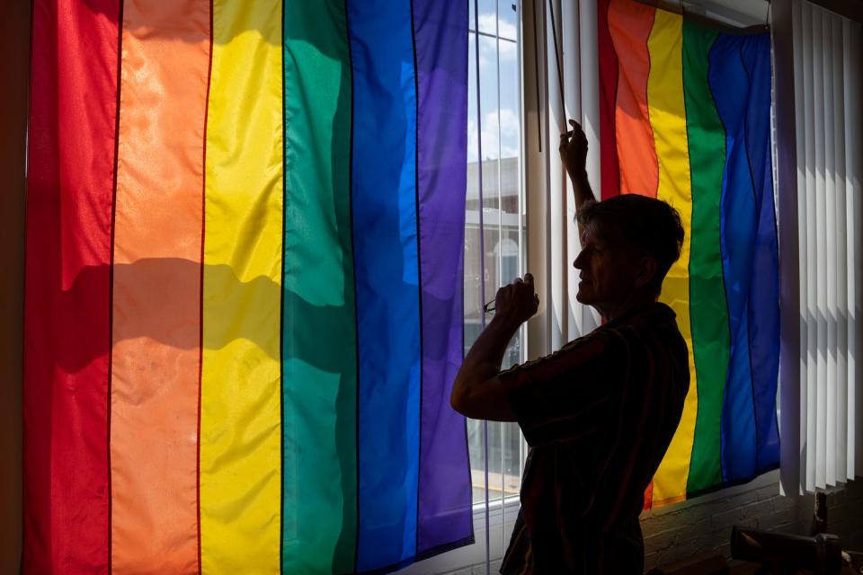 Tracy Brown-Salsman, 57, closes the blinds on his porch, where three large rainbow flags hang, on Thursday, July 14, 2022. Tracy and his husband Tim live in Loogootee.