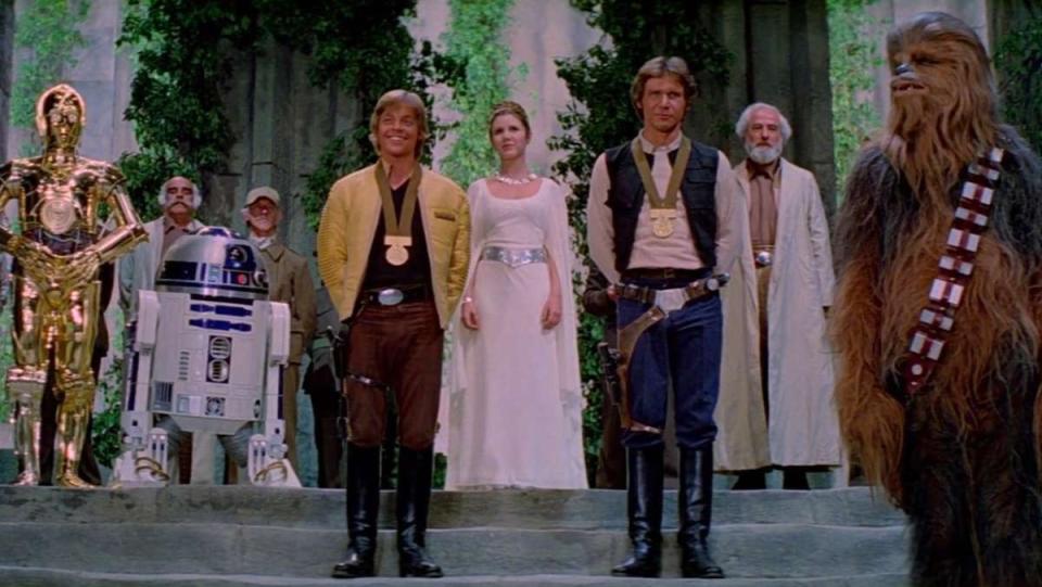 A shot of all of our heroes from the medal ceremony scene from Star Wars: A New Hope. From left, C-3PO, R2-D2, Luke Skywalker, Princess Leia, Han Solo, General Jan Dodonna, and Chewbacca. Only Han and Luke have medals for some reason.