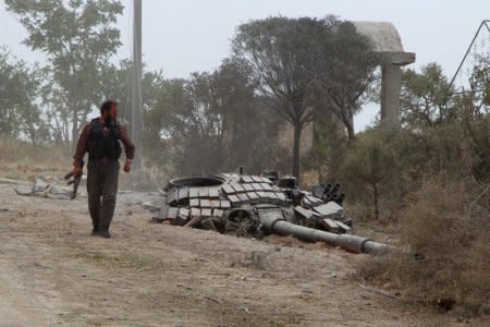 FILE PHOTO: A rebel fighter carries his weapon as he walks past the turret of a damaged tank at the Mastouma military base, after they seized it, in Idlib May 20, 2015. REUTERS/Ammar Abdullah/File Photo