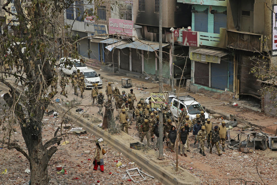 FILE- In this Thursday, Feb. 27, 2020, file photo, an Indian woman walks past as Indian paramilitary soldiers patrol a street vandalized in Tuesday's violence in New Delhi, India. Facebook in India has been selective in curbing hate speech, misinformation and inflammatory posts, particularly anti-Muslim content, according to leaked documents obtained by The Associated Press, even as the internet giant's own employees cast doubt over the motivations and interests.(AP Photo/Altaf Qadri,File)