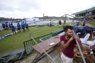 A fan waits holding on to a blown away spectator stand at Galle International Cricket Stadium on the day two of the first test cricket match between Australia and Sri Lanka in Galle, Sri Lanka, Thursday, June 30, 2022. (AP Photo/Eranga Jayawardena)