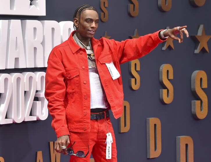 Soulja Boy In a loose red jacket and pants holding out his left arm and pointing in front of him