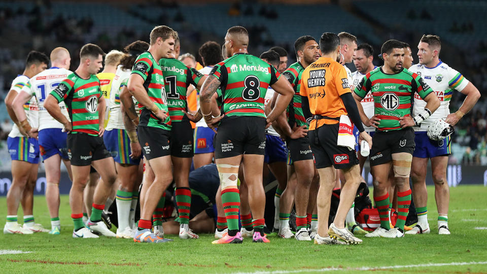 Raiders and Rabbitohs gather around Corey Harawira-Naera as he is attended to by doctors.