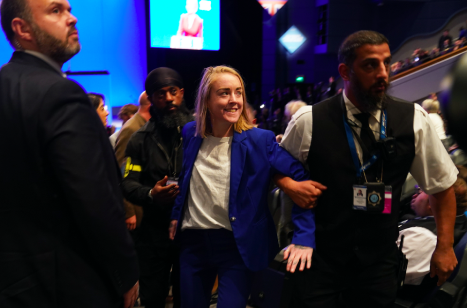 The protester is escorted out of the hall after she interrupted Liz Truss' speech. (PA)