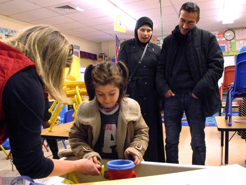 A newly arrived Syrian refugee plays in a classroom as her parents watch