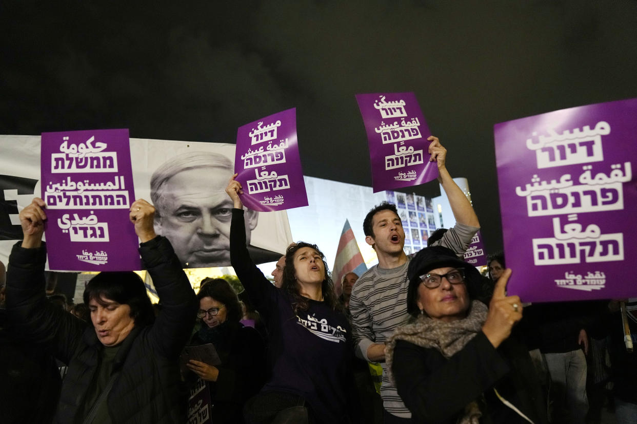 Activists chant slogans in Tel Aviv, Israel, to protest against Prime Minister Benjamin Netanyahu's far-right government, Saturday, Jan. 7, 2023. The placard at left reads: "The settler government is against me."; the placard at right reads: "housing, livelihood, hope." (AP Photo/ Tsafrir Abayov)