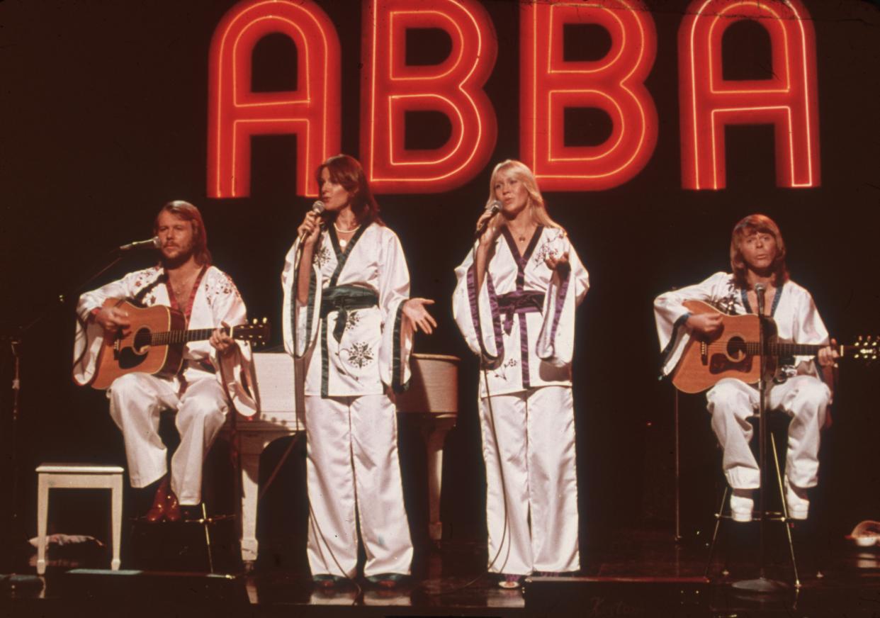 circa 1975:  Swedish pop group ABBA (L-R: Benny Andersson, Frida Lyngstad, Agnetha Faltskog, Bjorn Ulvaeus), wearing similar white Asian-influenced costumes, perform for the television program Midnight Special with a neon 'ABBA' sign in the background.  (Photo by Hulton Archive/Getty Images)
