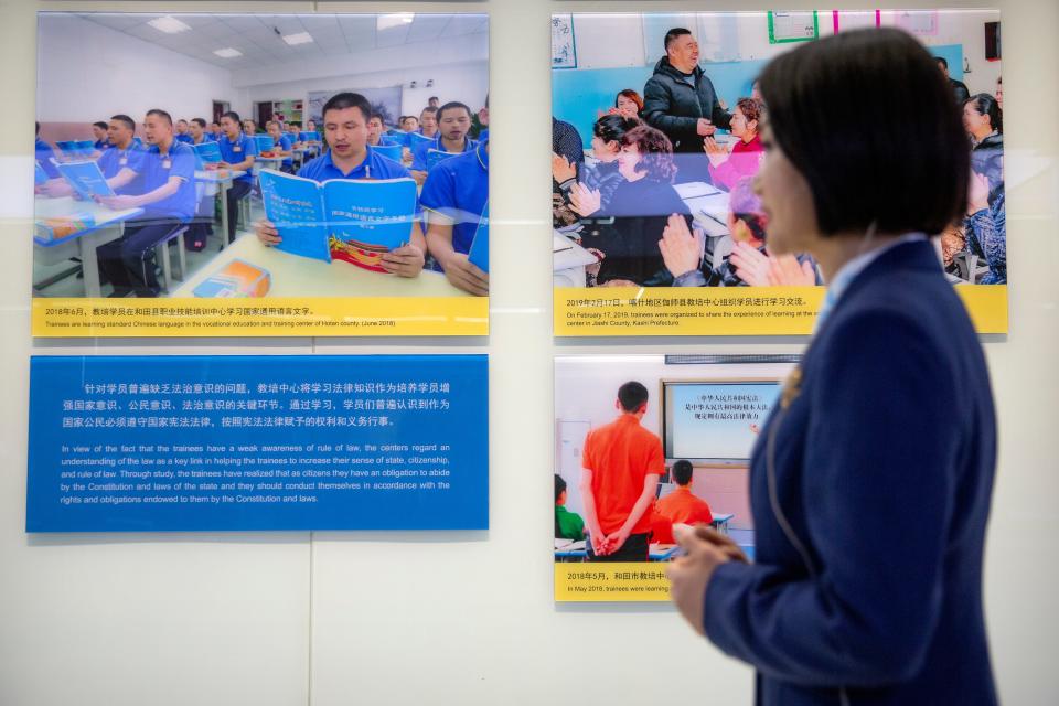 A tour guide stands near a display showing images of people at locations described as vocational training centers in southern Xinjiang at the Exhibition of the Fight Against Terrorism and Extremism in Urumqi in western China's Xinjiang Uyghur Autonomous Region on April 21, 2021.