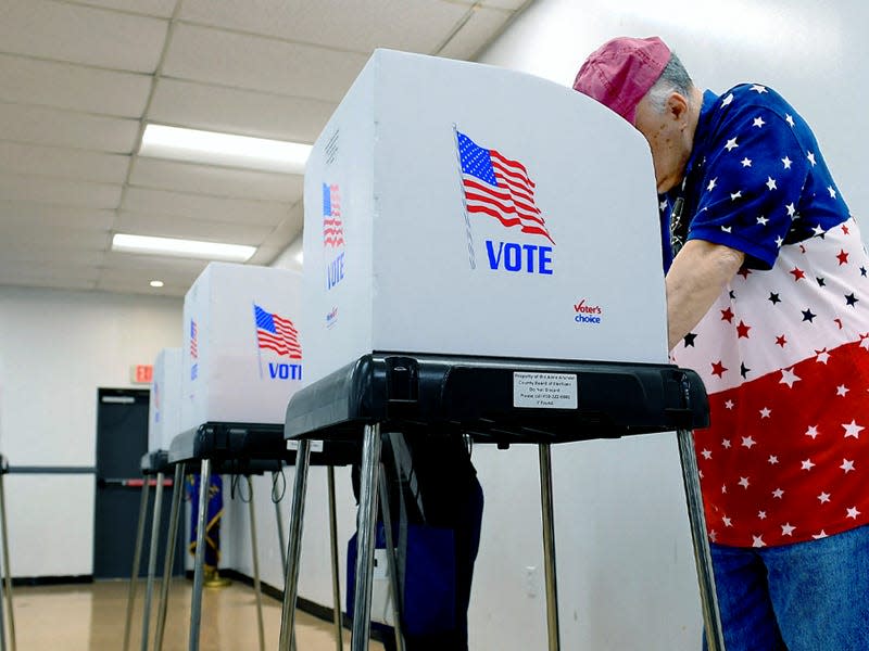 Man in a red, white, and blue shirt voting in a voting center for 2022 midterm elections.
