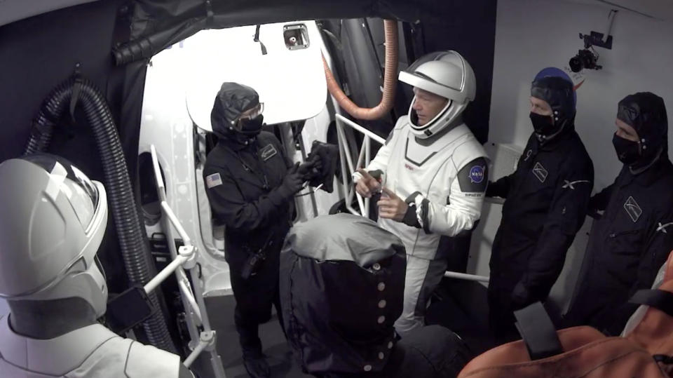 In this Wednesday, May 27, 2020 image from video made available by SpaceX, NASA astronauts Doug Hurley, center, and Bob Behnken, left, confer with technicians after leaving the Crew Dragon capsule at the Kennedy Space Center in Cape Canaveral, Fla., after an aborted launch due to weather problems. (SpaceX via AP)