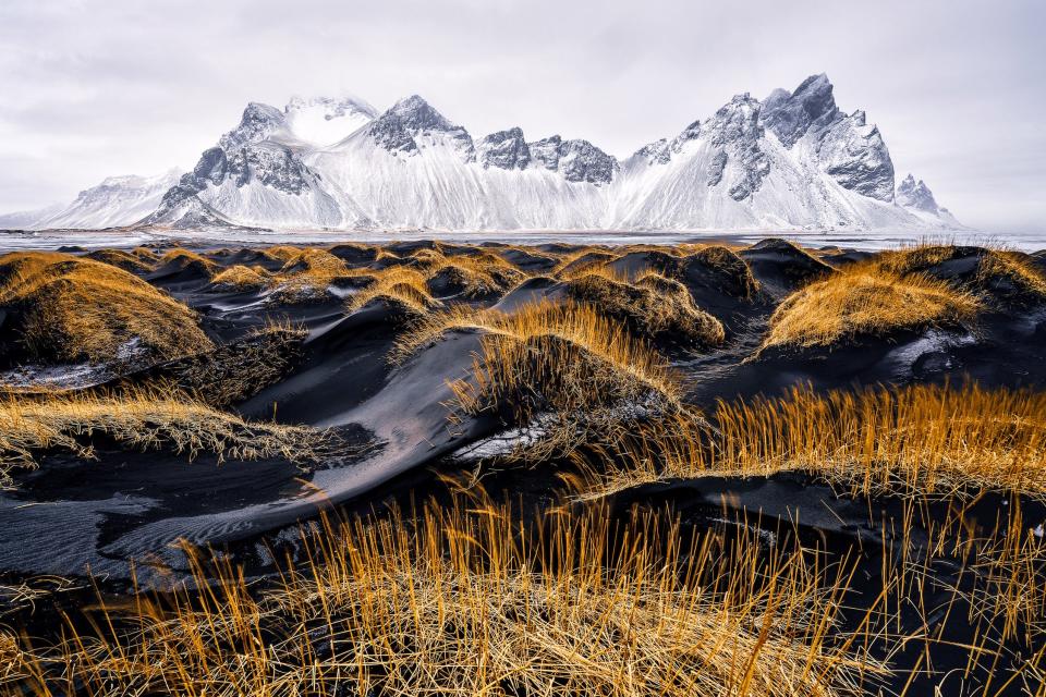 black sand beach with orange grass snowy white mountain in background