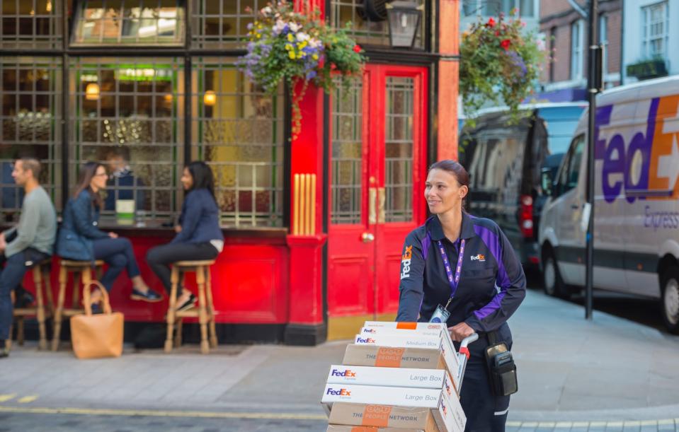 Female FedEx driver delivering packages in front of a restaurant with outdoor seating.