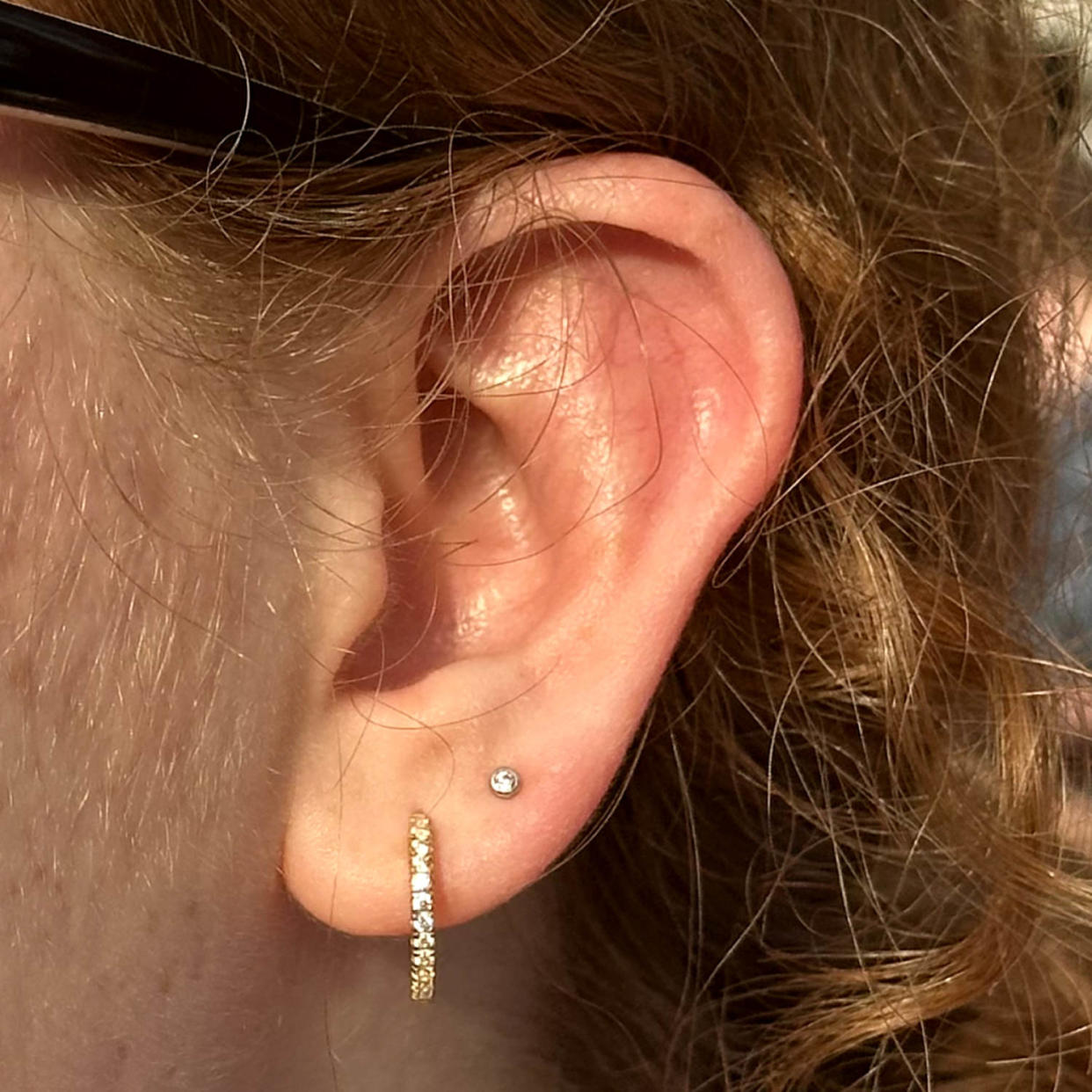 A woman pairs thin, gold, crystal-lined Rowan CZ 11mm Hypoallergenic Hoops with a simple circular second piercing. (Courtesy Kelsey Fredricks, Production Coordinator)