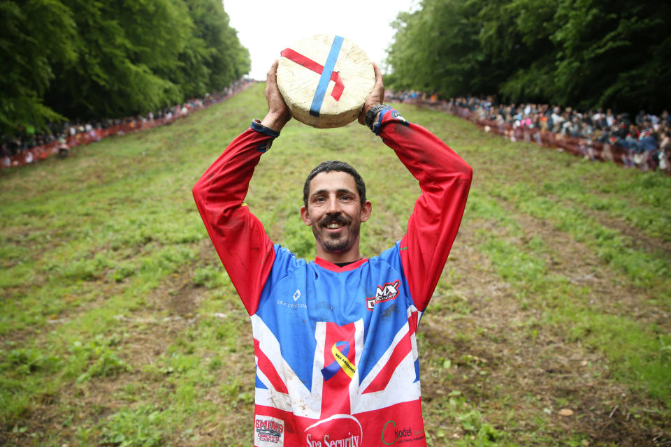 GLOUCESTER, ENGLAND - JUNE 05: Chris Anderson poses for a photo with the cheese after winning the first man's downhill race on June 05, 2022 in Gloucester, England. The Cooper's Hill Cheese-Rolling and Wake annual event returns this year after a break during the Covid pandemic. It is held on the Spring Bank Holiday at Cooper's Hill, near Gloucester and this year it happens to coincide with the Queen's Platinum Jubilee. Participants race down the 200-yard-long hill after a 3.6kg round of Double Gloucester cheese. (Photo by Cameron Smith/Getty Images)