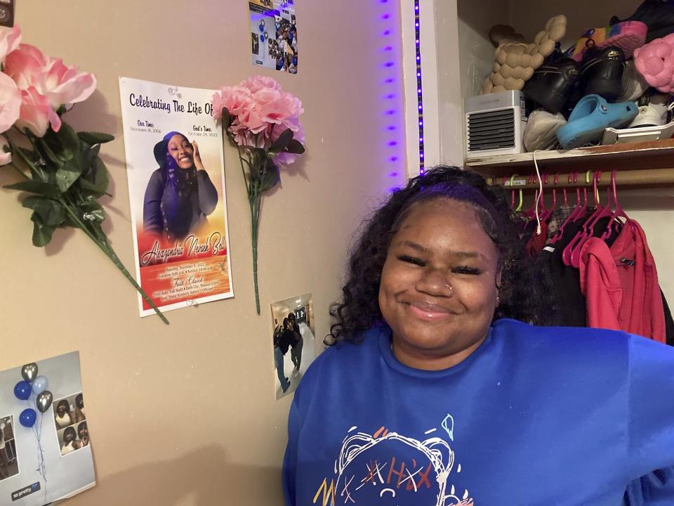 McKynzi Douglas stands next to a memorial poster of her friend Alexzandria Bell, displayed in her home in St. Louis, Mo., on Thursday, Jan. 26, 2023. Douglas fled without injury, but Bell was killed in an Oct. 24 shooting at Central Visual and Performing Arts High School in St. Louis. (AP Photo/Jim Salter)