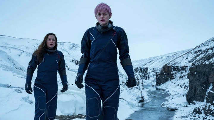 Darby and Sian walking in snowsuits with a wintery scene from A Murder at the End of the World.