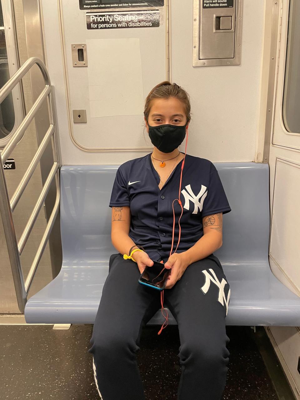 The author, in full Yankee attire, sits on a subway in NYC.