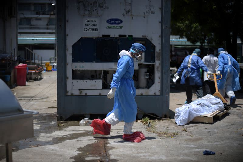 Health workers wearing protective gear bring a dead body past a refrigerated container outside of Teodoro Maldonado Carbo Hospital amid the spread of the coronavirus disease (COVID-19), in Guayaquil