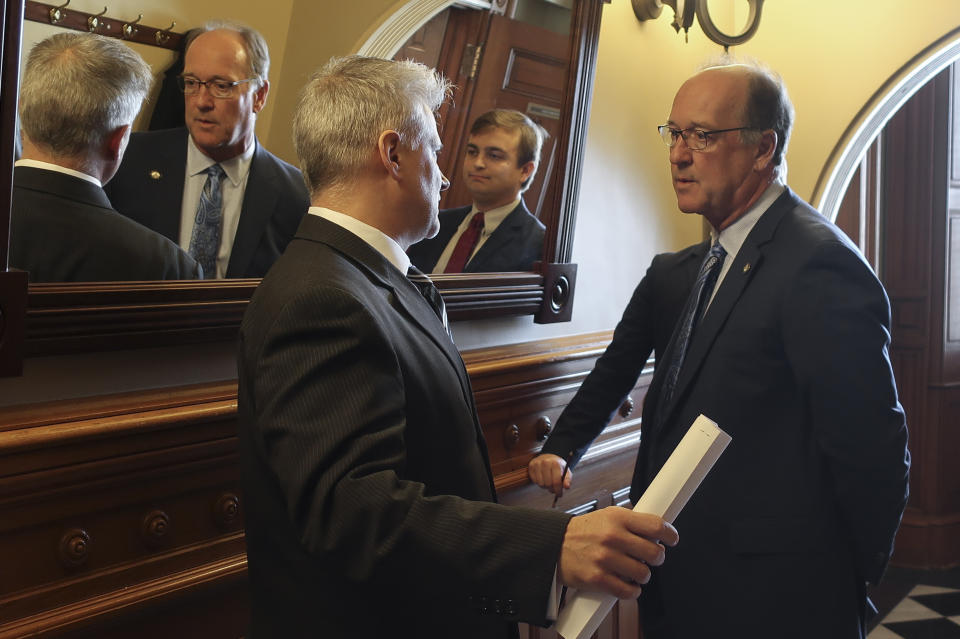 Tim Graham, left, a member of Kansas Gov. Laura Kelly's staff, confers with Senate Vice President Jeff Longbine, right, R-Emporia, outside the Senate chamber ahead of a debate on legalizing betting on sports events, Wednesday, Feb. 26, 2020, at the Statehouse in Topeka, Kan. Pictured between them in the mirror is Michael Murray, Longbine's chief of staff. (AP Photo/John Hanna)