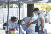 A passenger of a bus coming from Romania, right, undergoes a voluntary Covid-19 blood test, at the Tiburtina bus station, in Rome, Wednesday, July 29, 2020. The Lazio region, which includes Rome, is beginning voluntary tests on passengers arriving in Italy from Romania, Bulgaria and Ukraine, with a blood test on finger with results in 8 minutes followed by swab test if result is positive. (AP Photo/Riccardo De Luca)